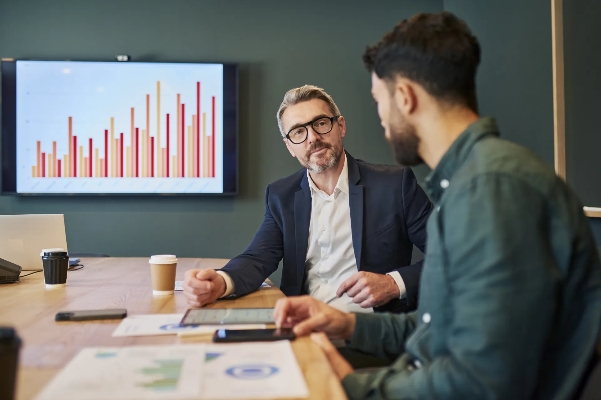 Personen in gesprek met scherm met diagrammen in achtergrond